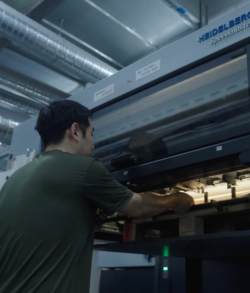 Technician operating Heidelberg offset printing press during full-color production run