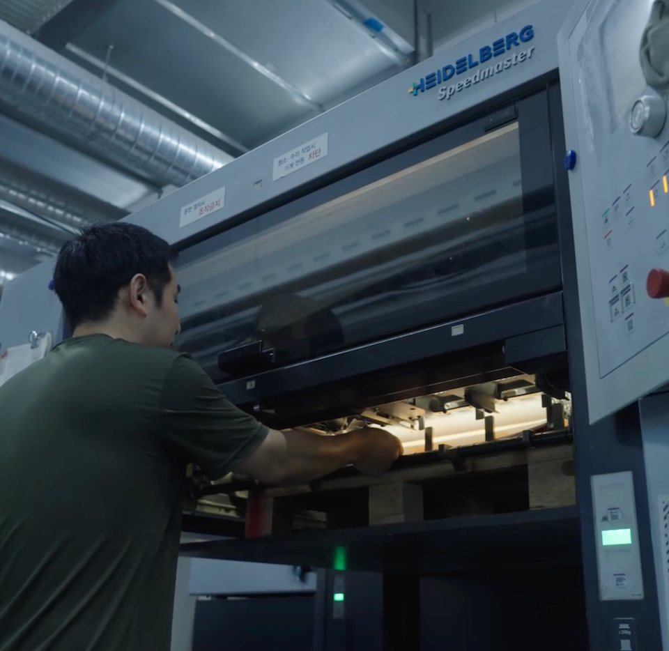 Print technician pulling a freshly printed sheet from a Heidelberg press for quality inspection at the inclpress facility